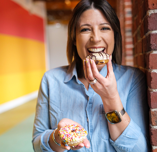 Owner of Planted Donuts, Julie Freitas eating a Planted Donut with a smile.